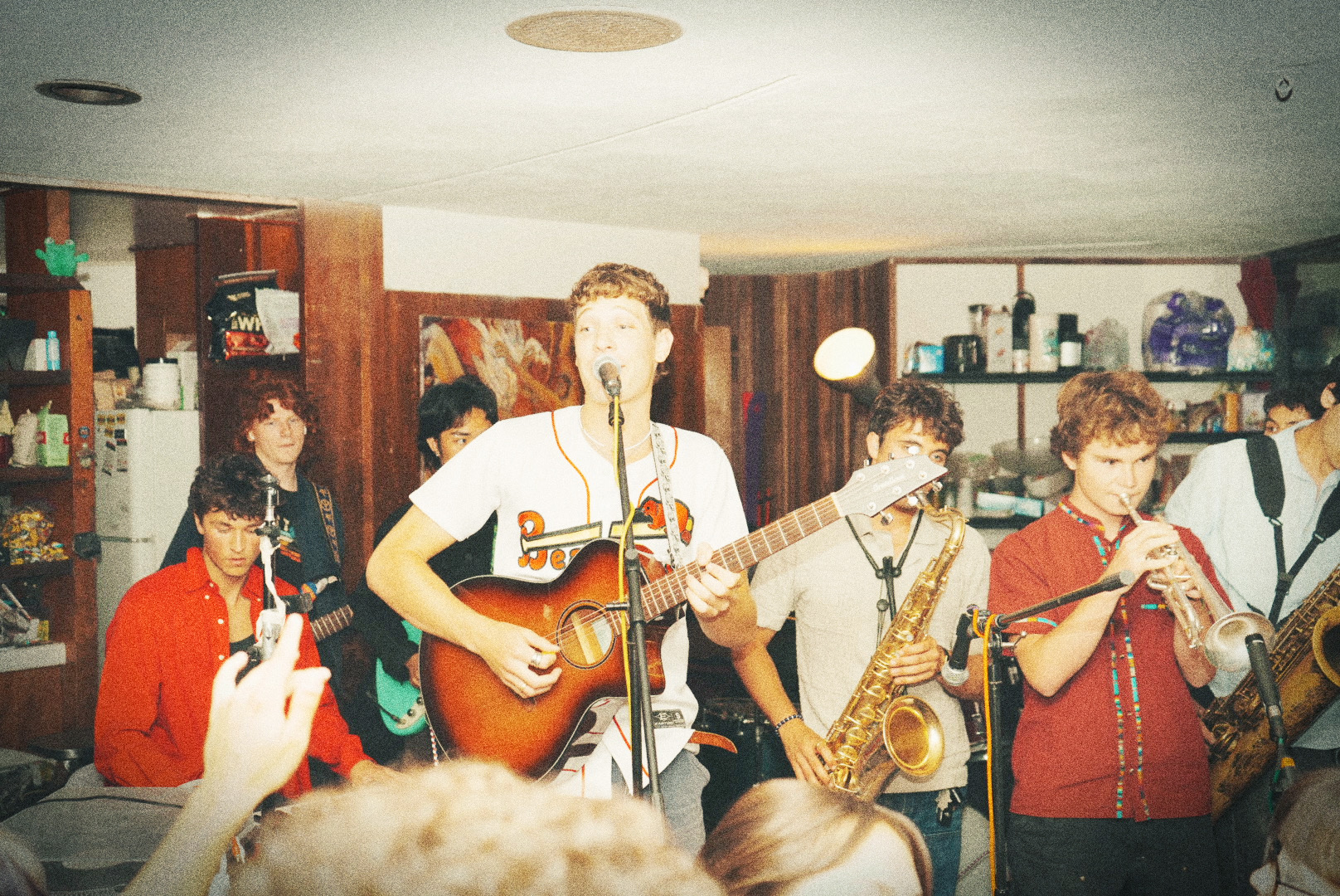 Singer with an acoustic guitar leading the band at a packed house party