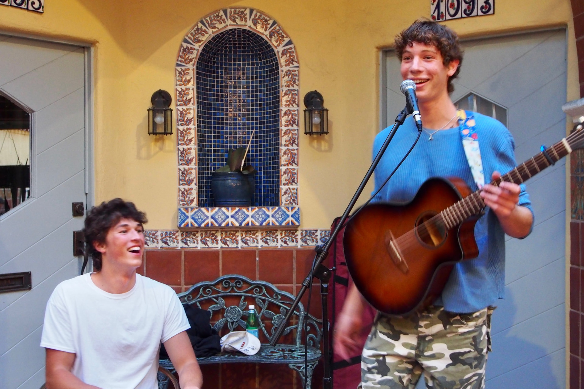 Two members playing acoustic guitar in a sunny courtyard