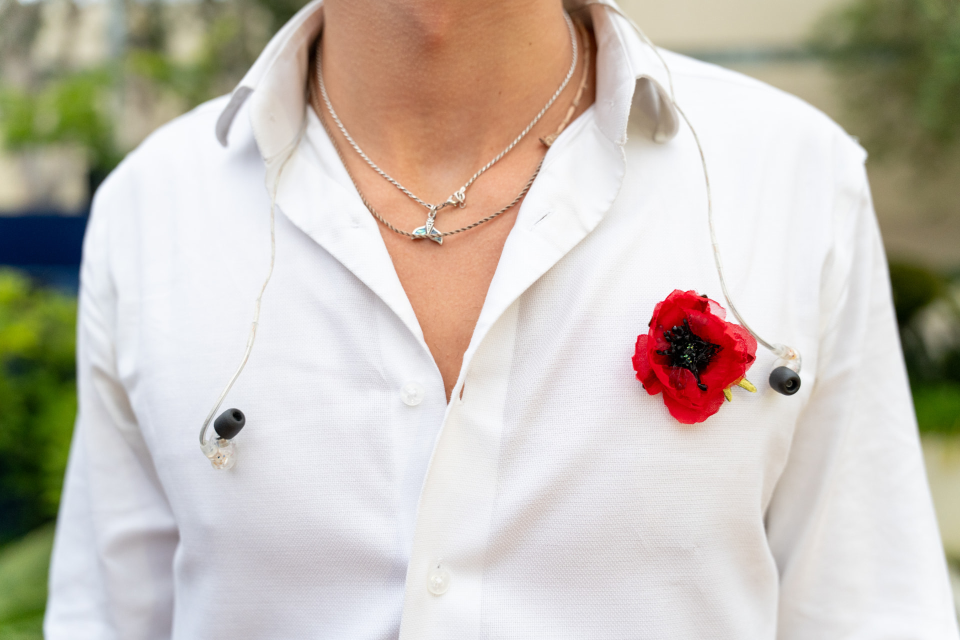 Detail of a red poppy pinned to a white shirt with in-ear monitors