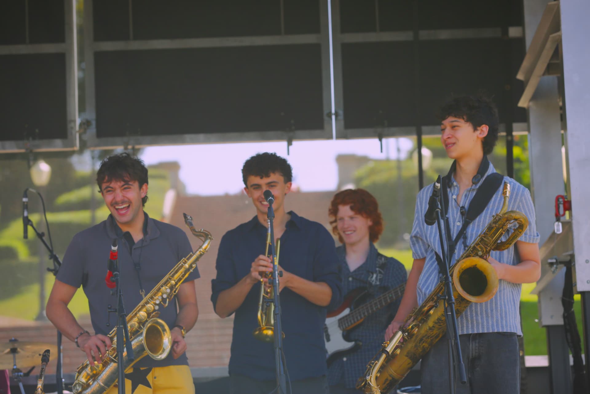 Horn section and bassist laughing during an outdoor daytime set